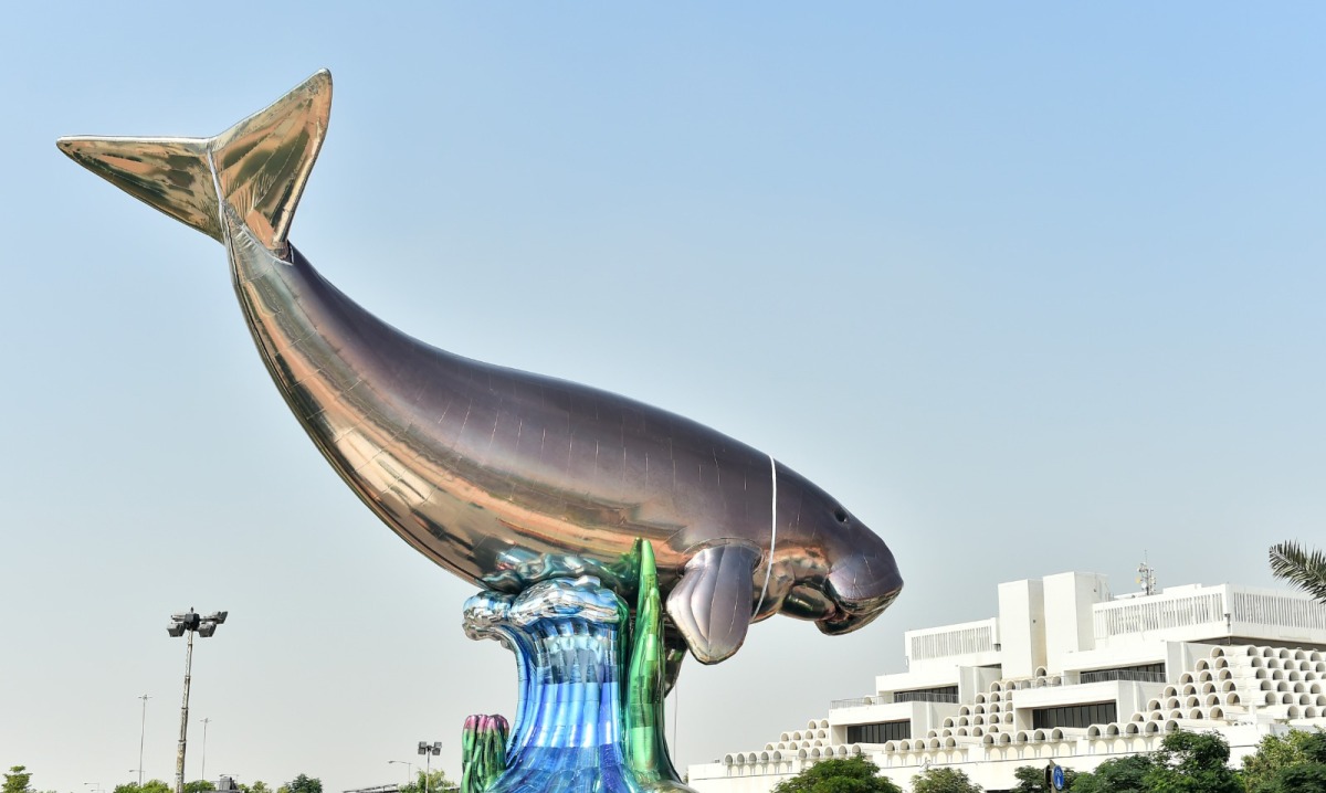 Escultura de Jeff Koons de acero inoxidable policromado con pulido espejo, con la forma de una vaquita marina gigante sobre una ola y algas, que aborda el tema de la crisis climática